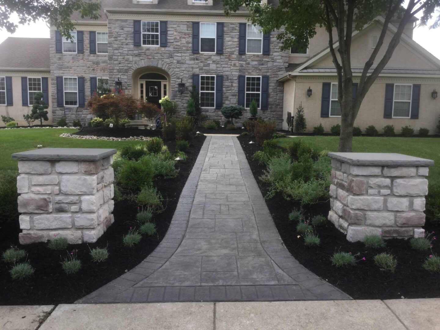 A walkway in front of a house with stone pillars.